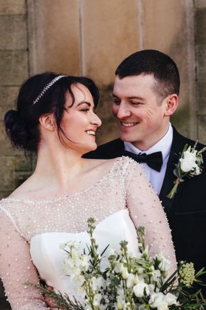 An intimate wedding portrait against stone architecture with white flowers.