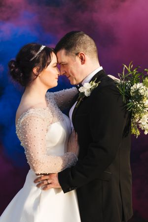 Intimate wedding portrait with dramatic pink and blue smoke effect background.