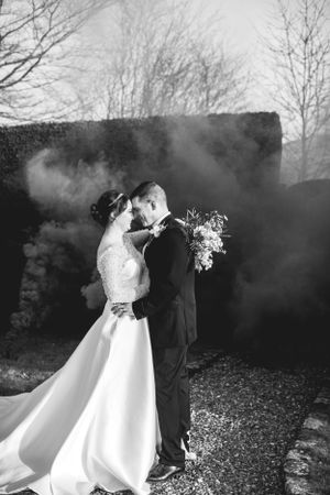Black and white wedding portrait with atmospheric smoke effects in garden setting.