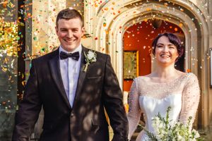 A couple exits a historic church during their wedding celebration as confetti falls around them.