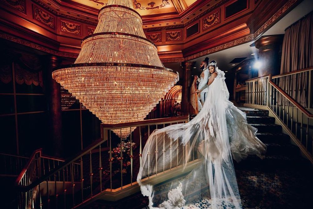 Elegant bridal portrait under grand crystal chandelier on ornate staircase.