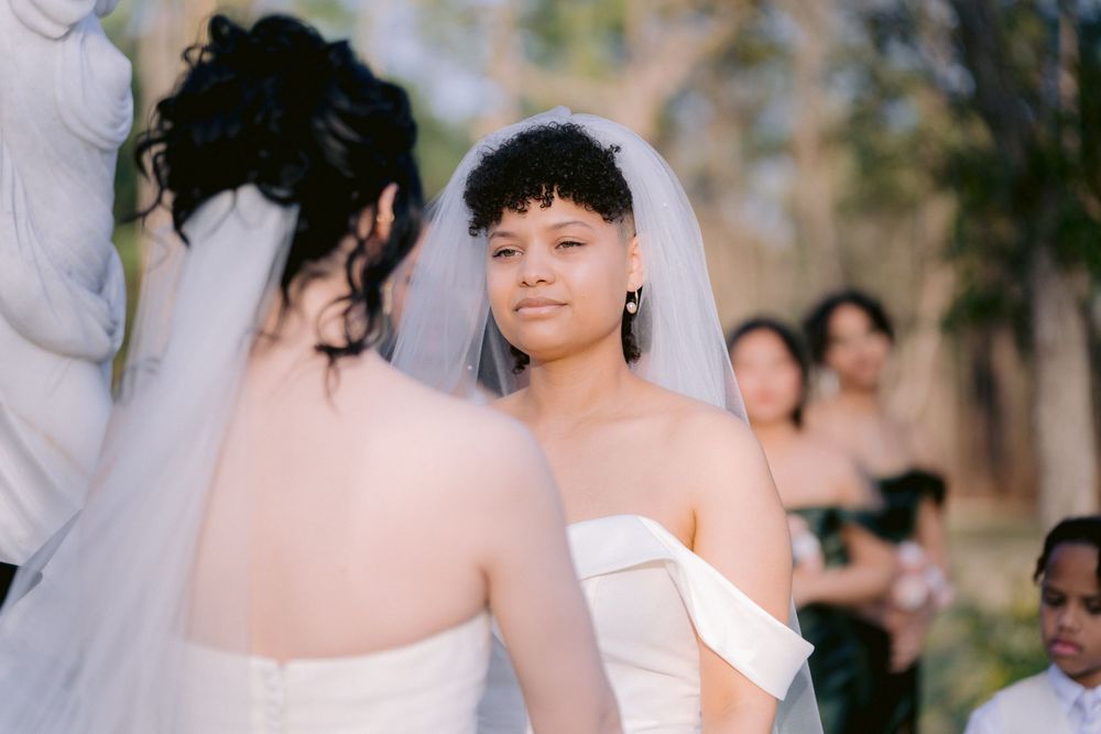 Two people in white wedding dresses sharing a moment during a ceremony.