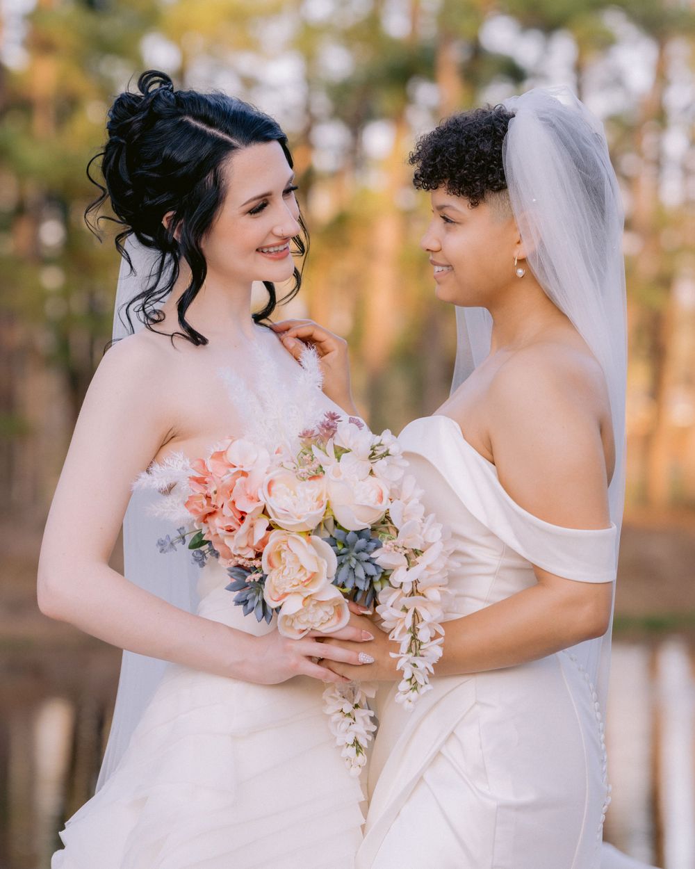 Two brides in white dresses share intimate moment while holding pink and white bouquet.