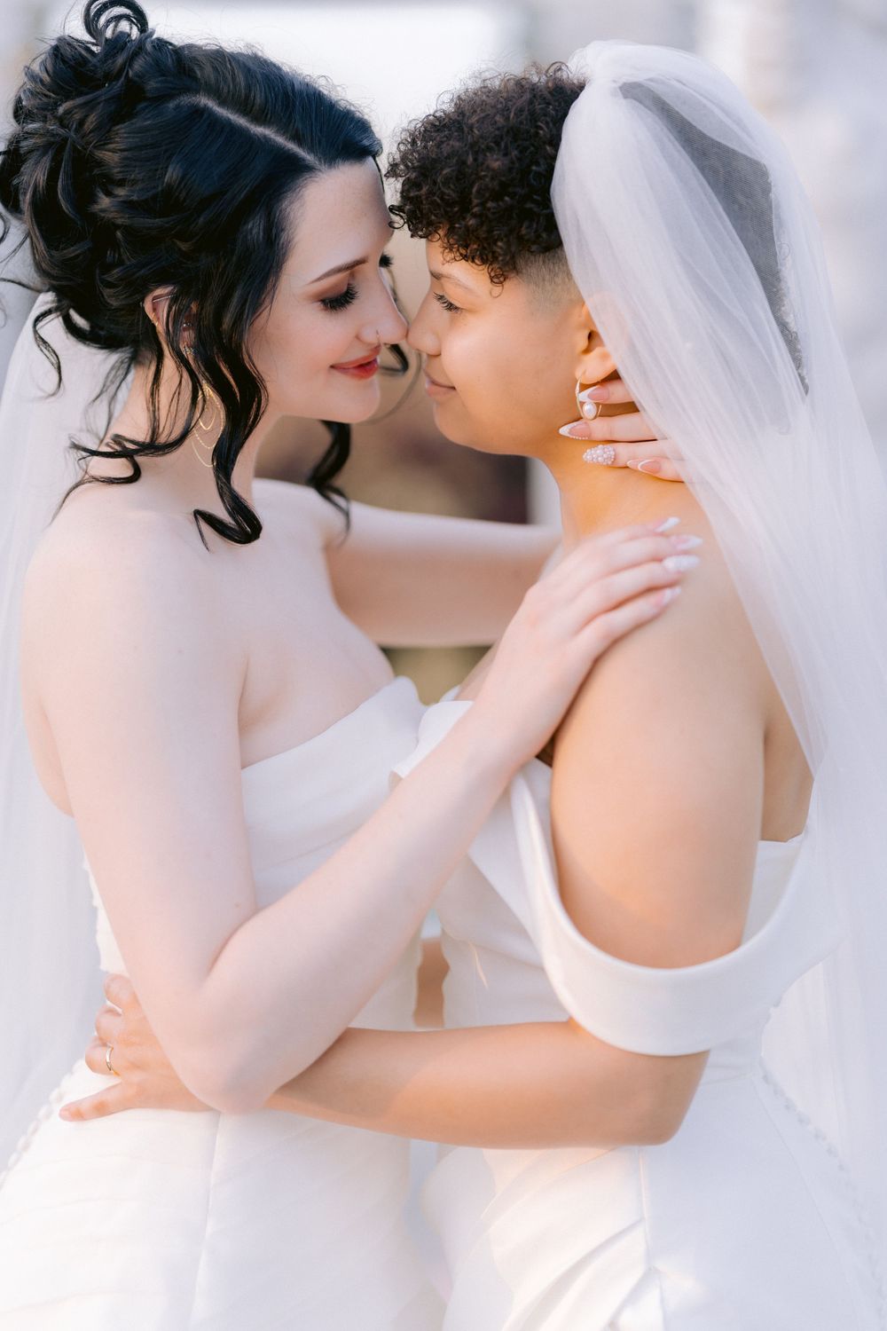 Intimate close-up of two brides in white dresses sharing tender moment.