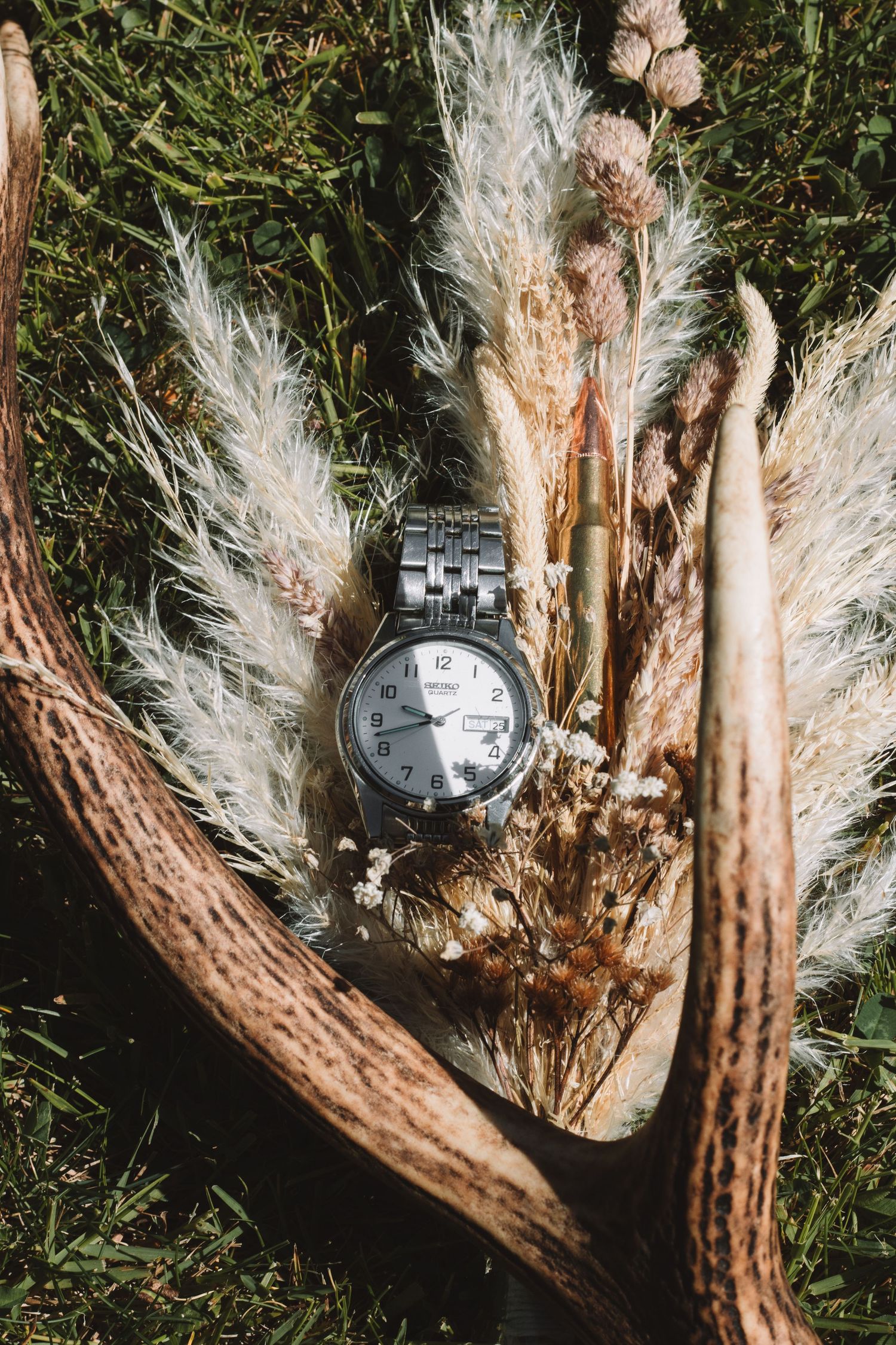 Silver watch displayed with dried pampas grass and antlers in natural lighting.