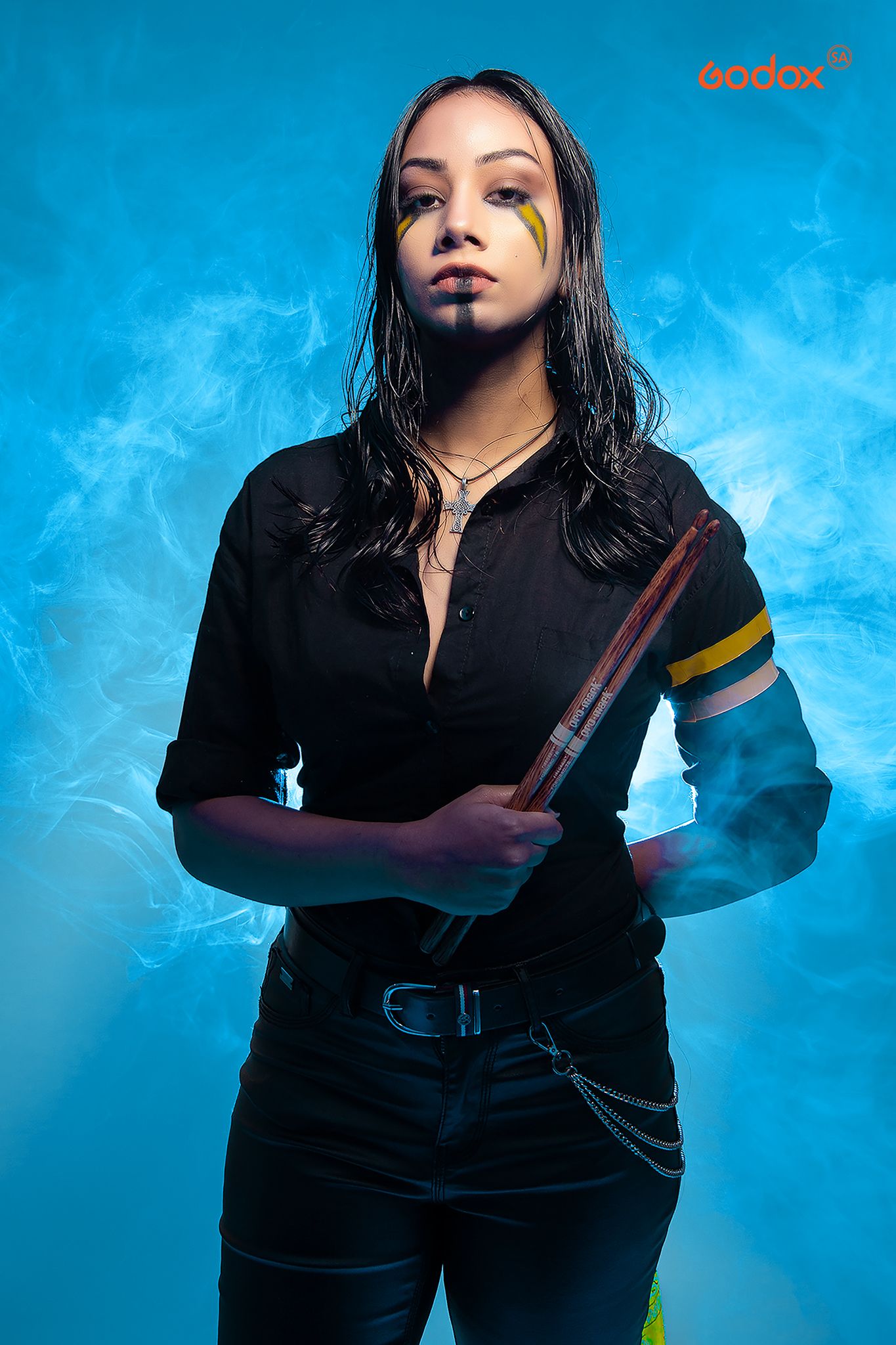 A figure in a black outfit poses dramatically against a vibrant blue background with smoky effects.