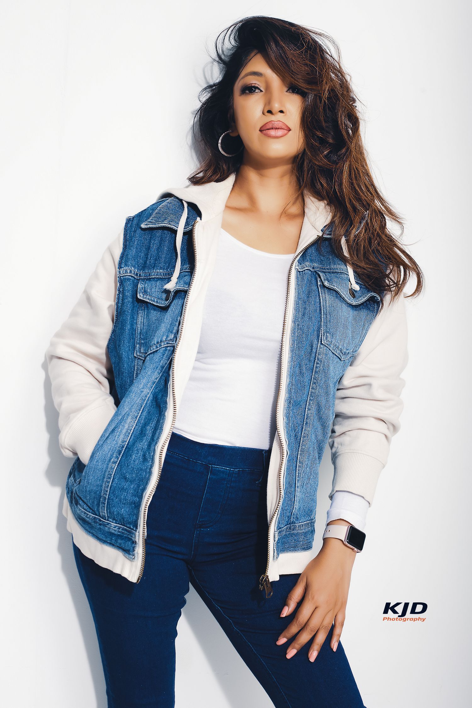 Woman poses in stylish denim jacket with jersey sleeves and matching pants against white background.
