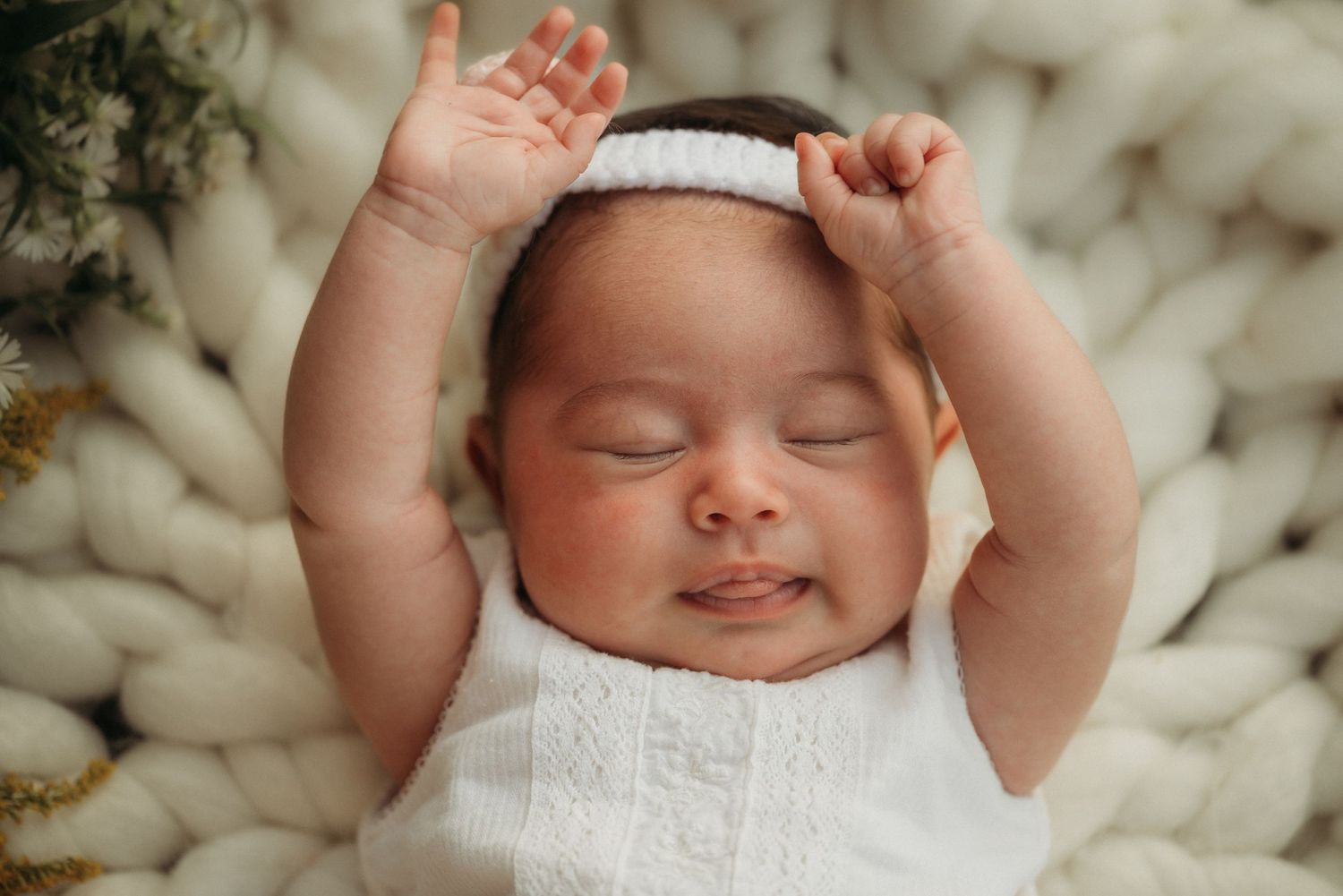 Peaceful baby stretching arms while sleeping on cozy white knit blanket.