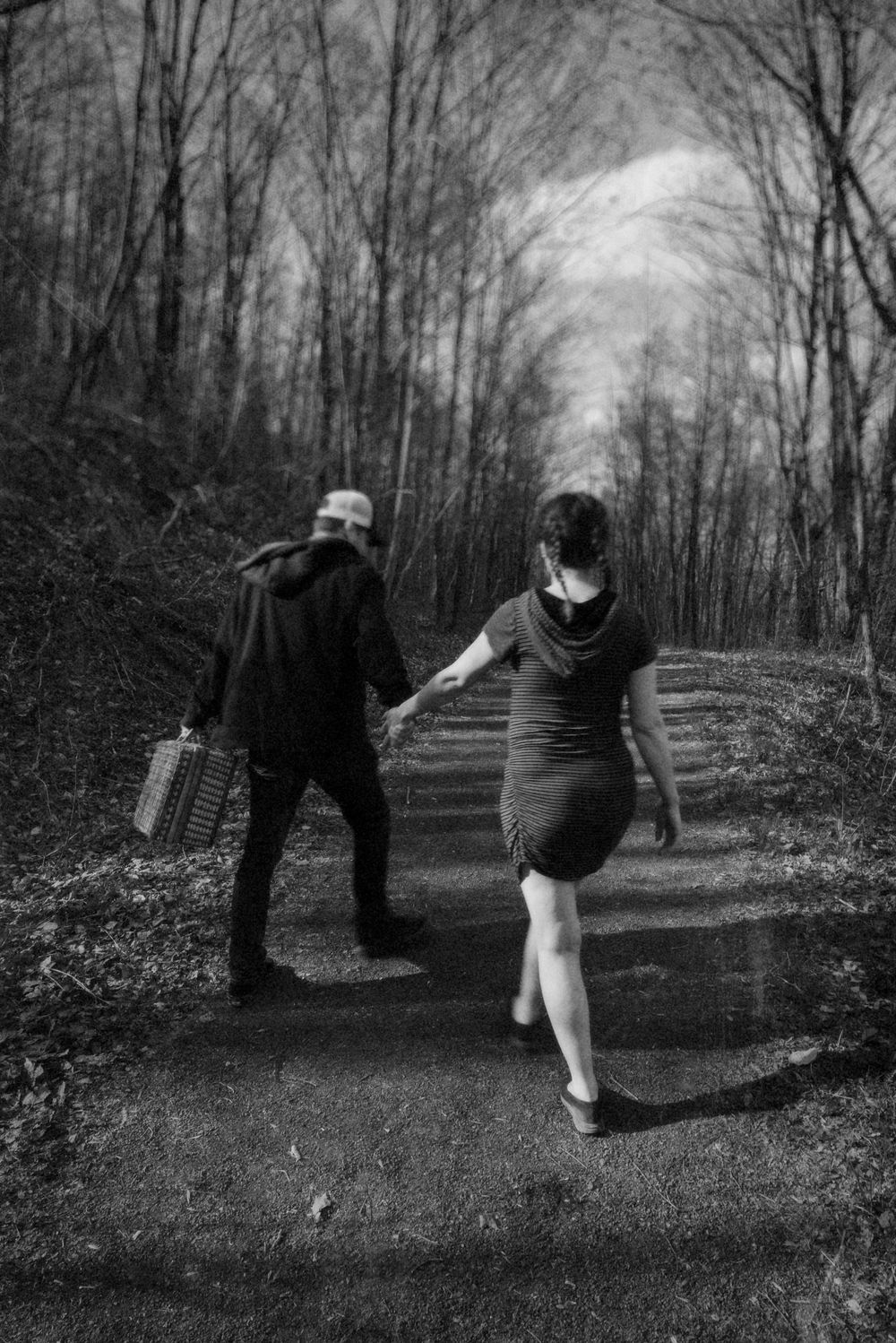 A black and white photo of a couple walking along a forest path carrying a picnic basket.