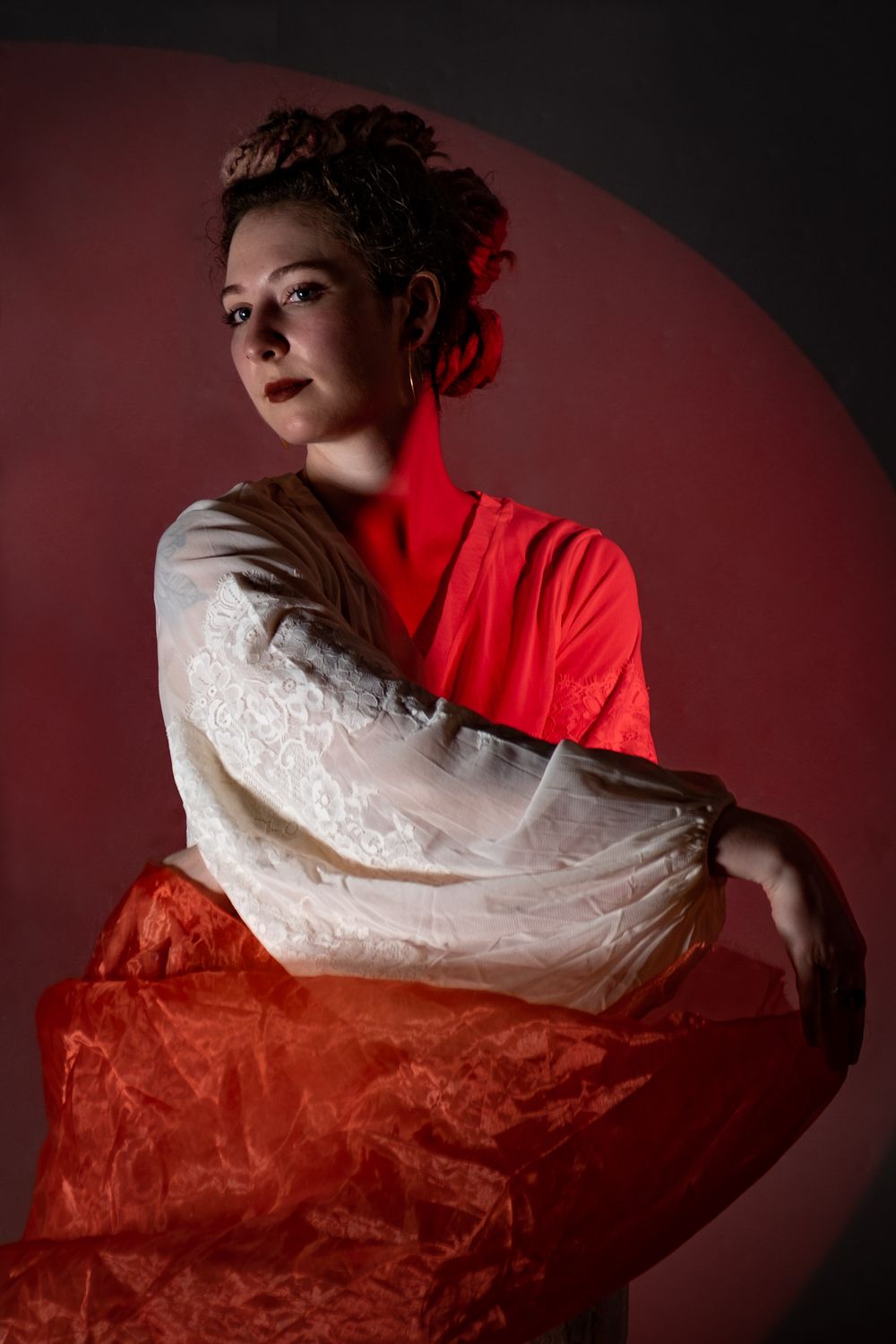 Dramatic portrait with red and white fabric creating flowing artistic composition against dark background.