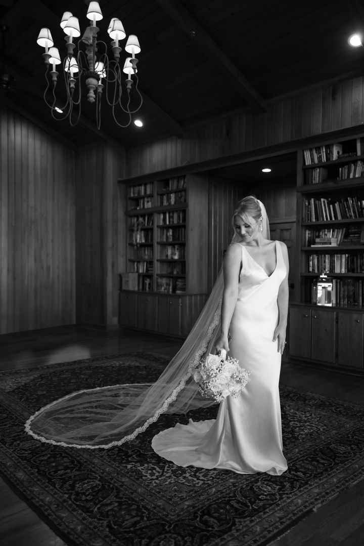 Classic black and white bridal portrait in a library setting with an elegant gown and long flowing veil.