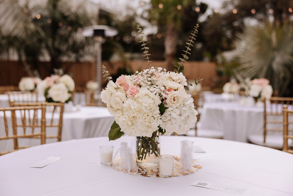 A delicate floral centerpiece with white and pink flowers in a glass vase on a round table at an elegant reception.