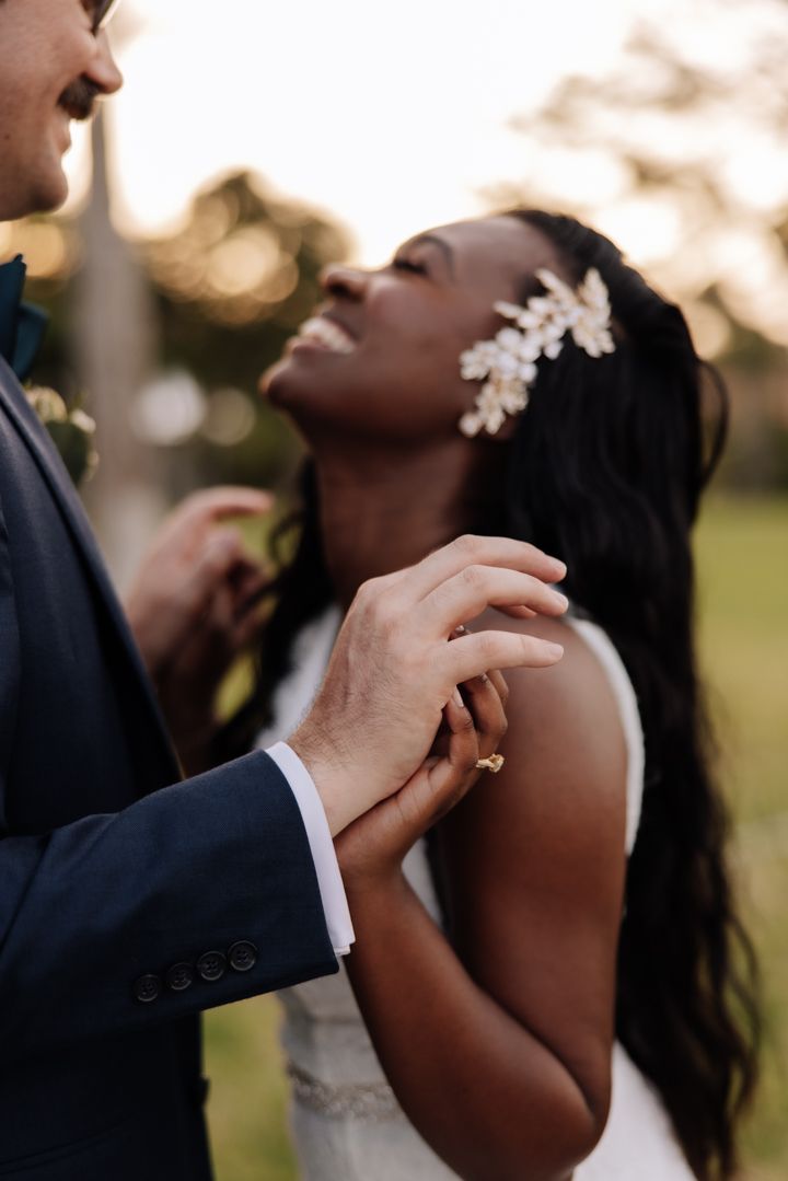 A tender moment between newlyweds at golden hour, with delicate floral hair piece and elegant navy suit.