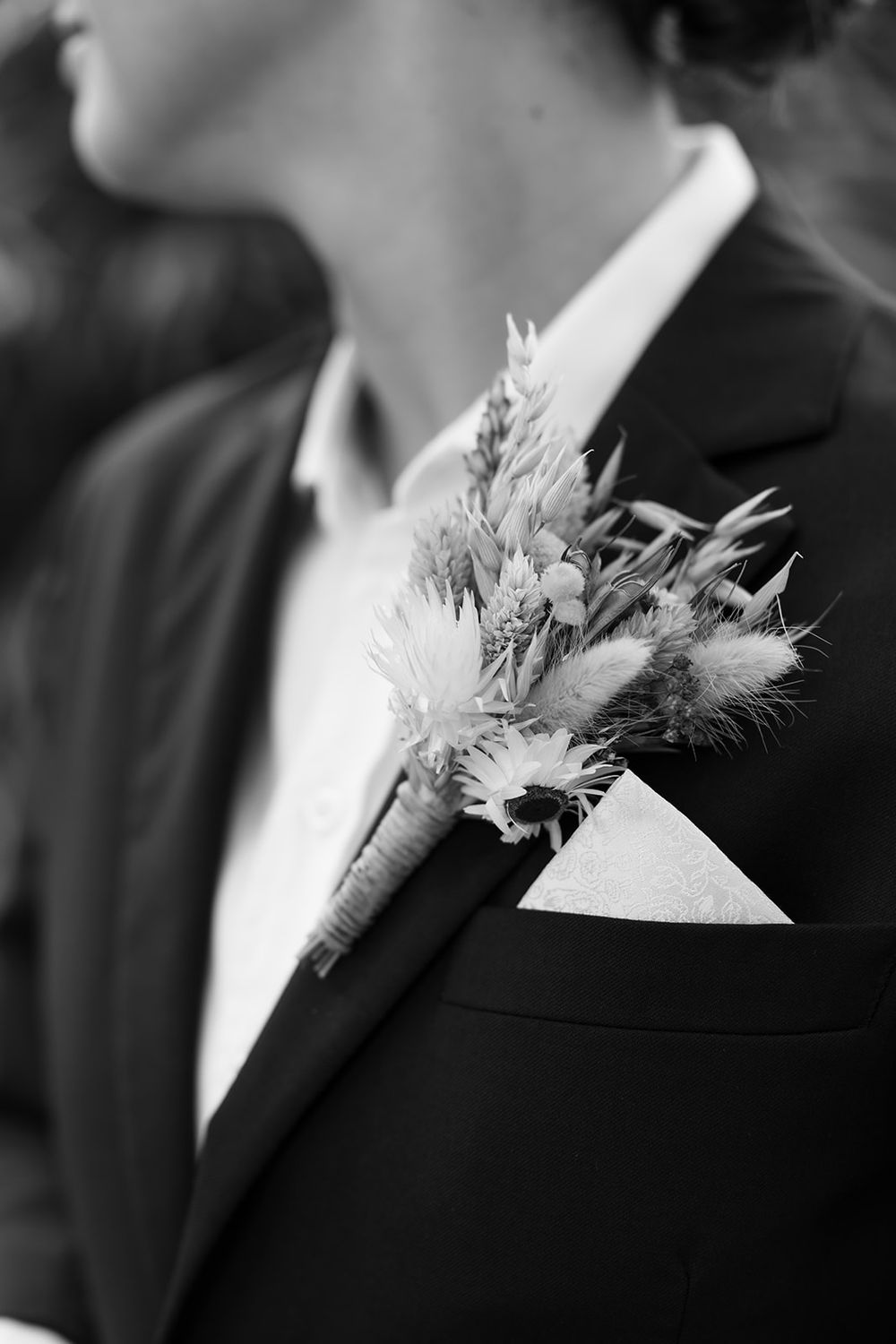 Four black and white close-up photos of formal suit lapels with delicate white floral boutonnieres.