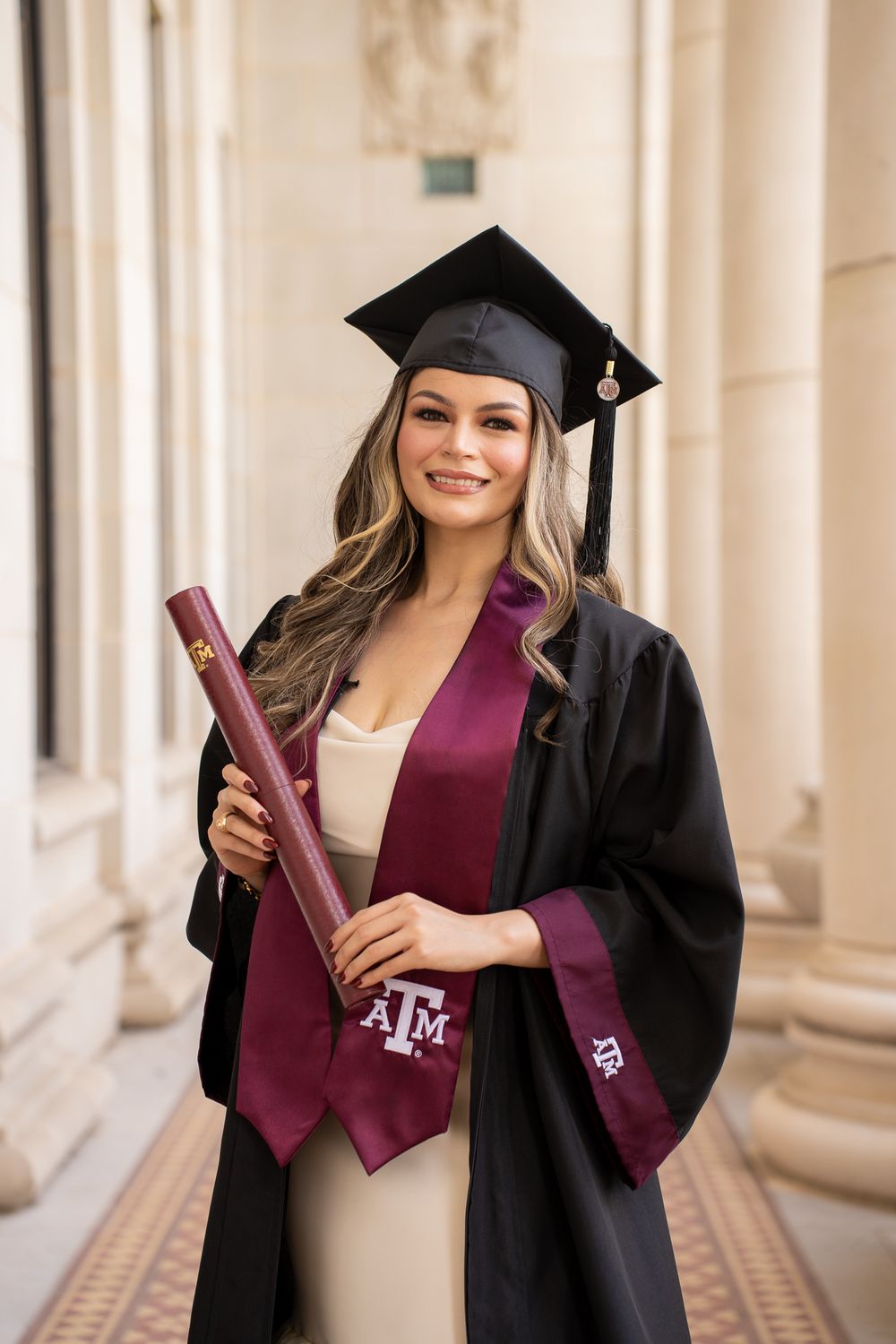 Graduate pictured in traditional black cap and gown with burgundy stole holding diploma from Texas A&M University.