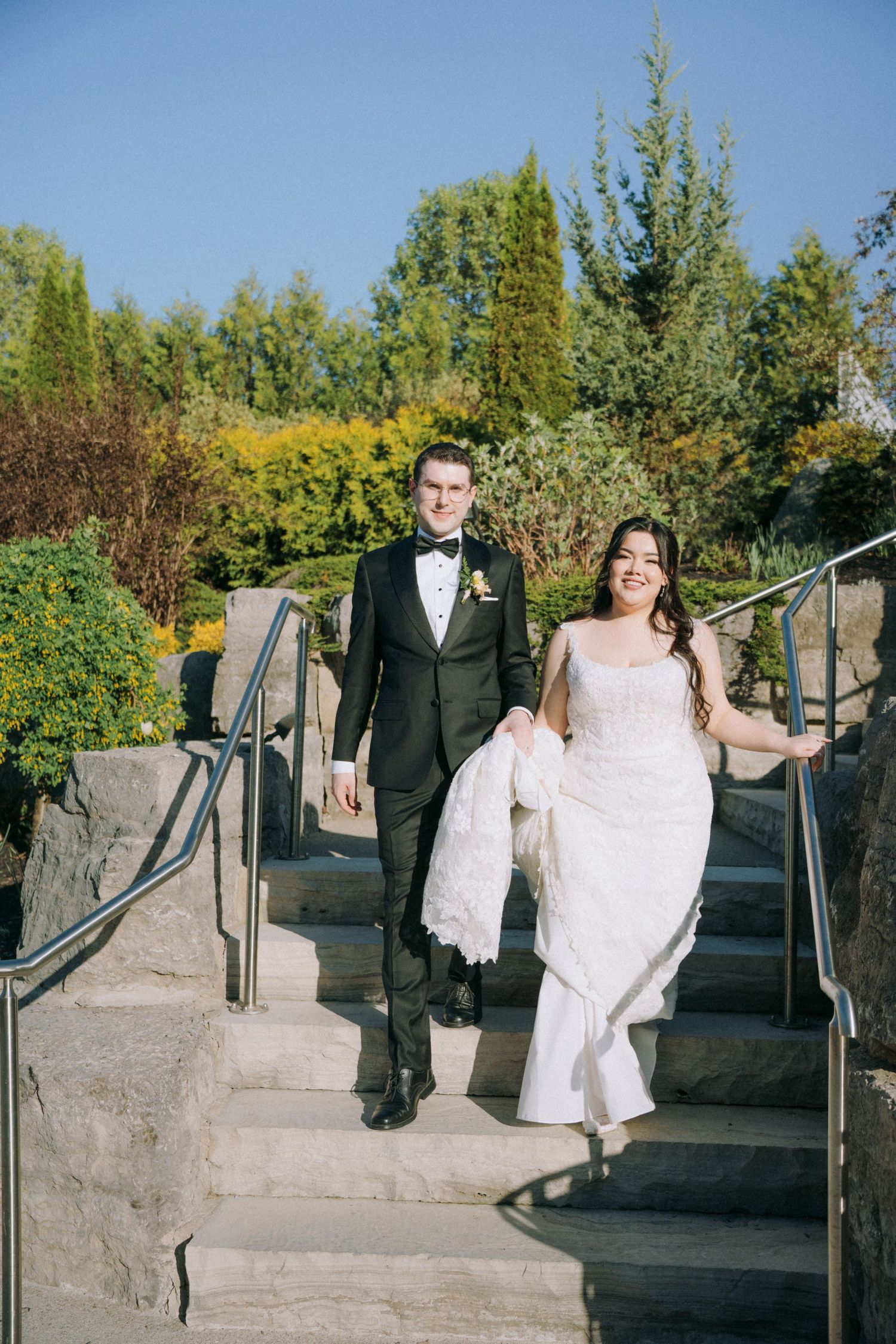 Wedding couple sitting on stone steps outdoors with the bride in white and groom in classic black tuxedo.