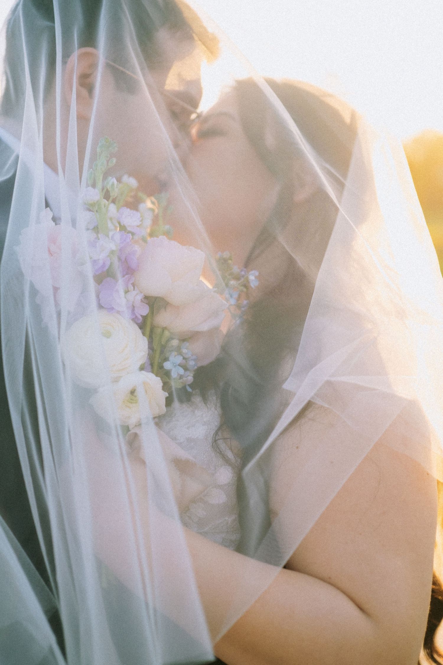 Romantic close-up wedding photo with soft sunlight filtering through a delicate white veil.