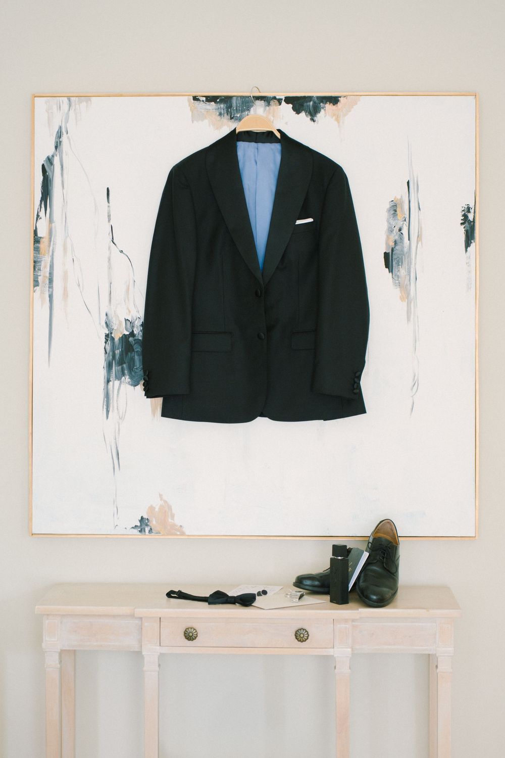 Black suit jacket hanging on wall above white console table with dress shoes.