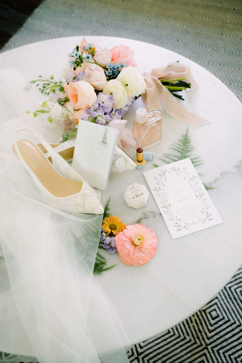 Wedding accessories including flowers, shoes, and invitation styled on a white surface.
