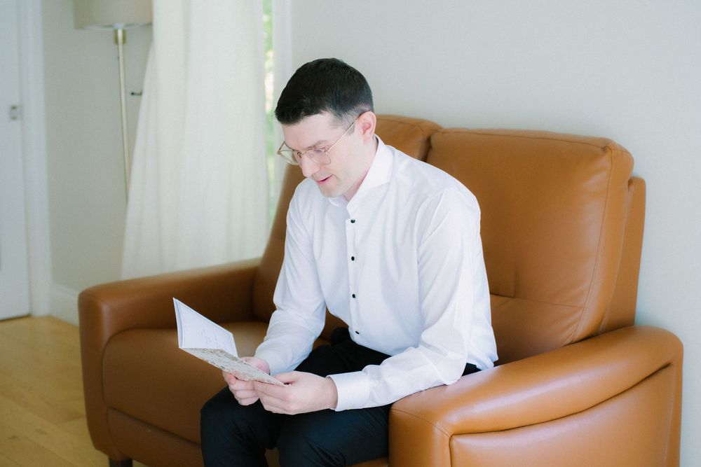 Person in white dress shirt reading document while seated in brown leather chair.