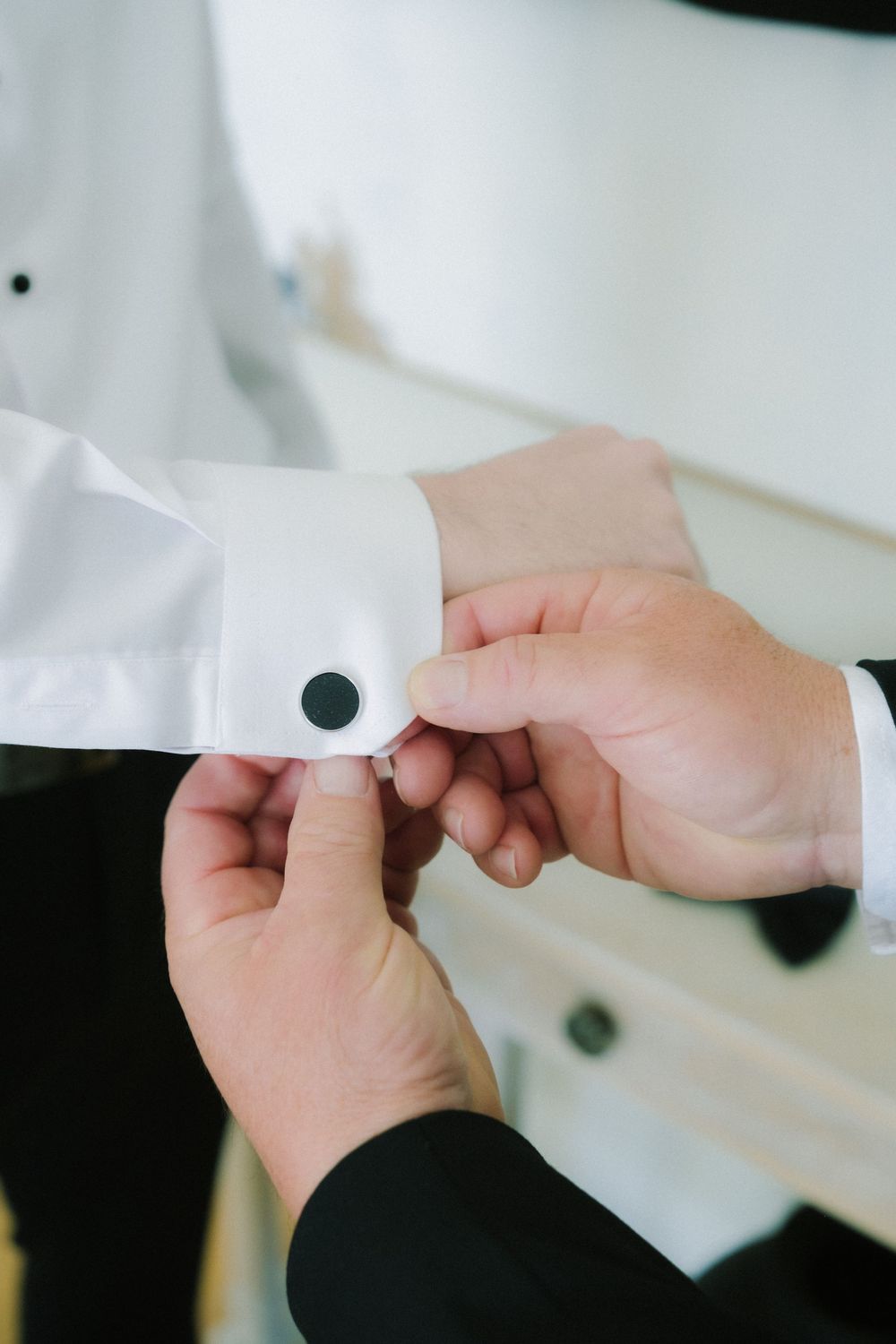 Close-up of hands fastening a white dress shirt cufflink.