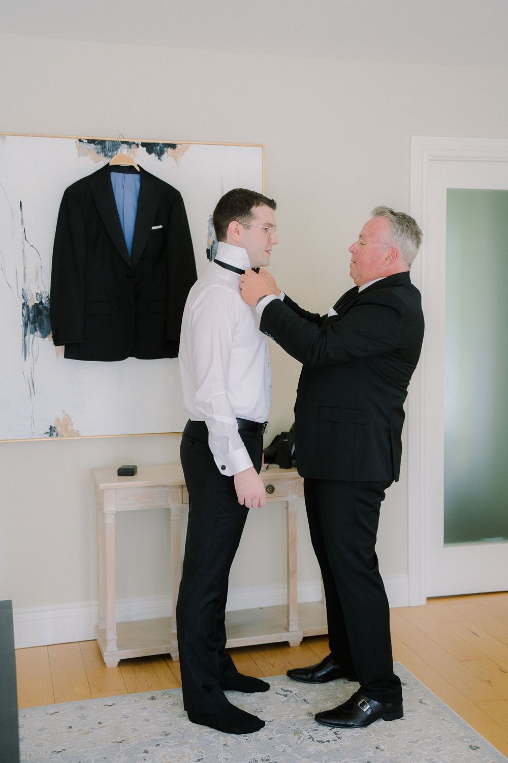 Two people adjusting formal attire in room with black jacket display.