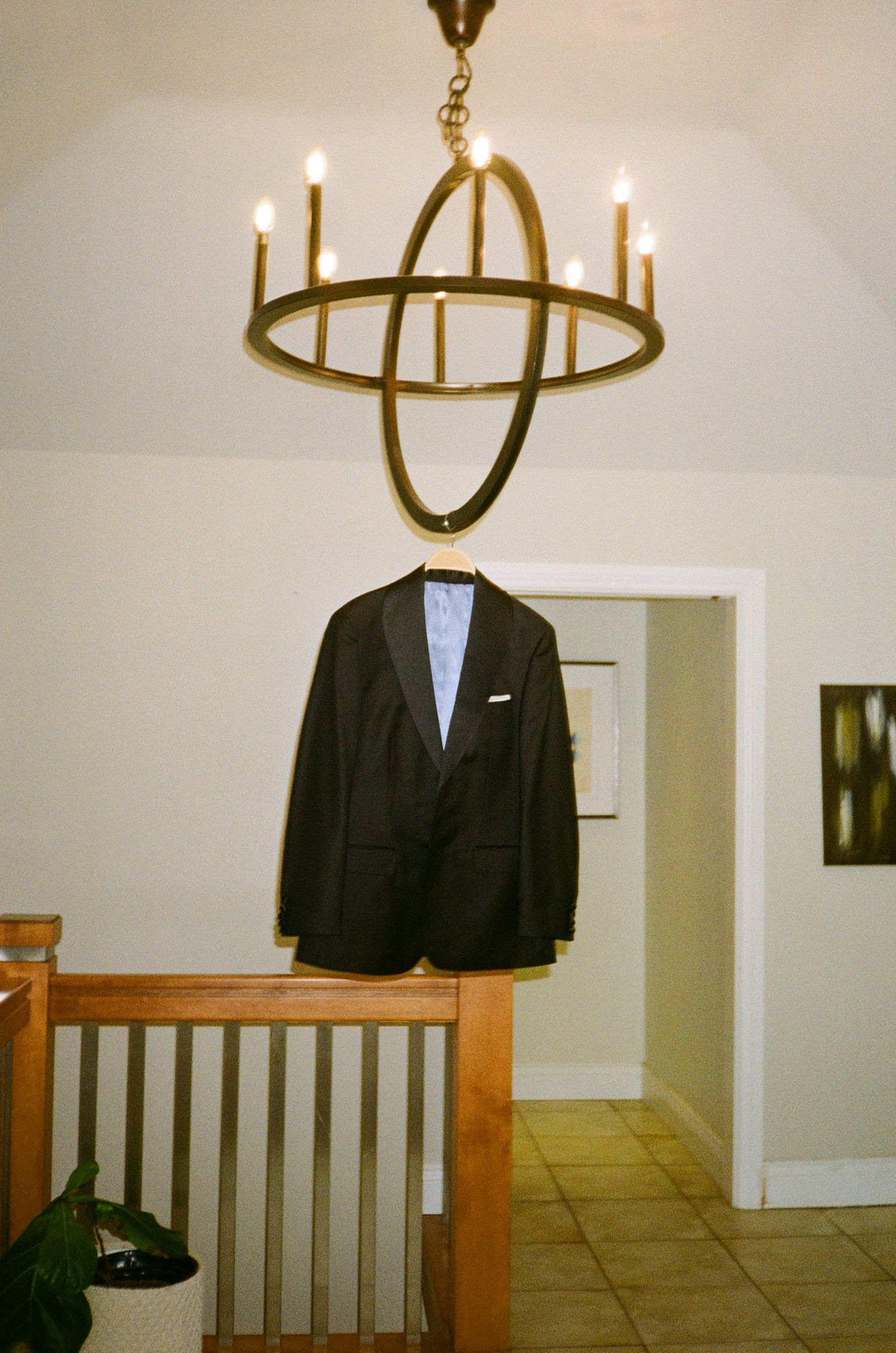 Black formal suit jacket hangs under an elegant gold chandelier in preparation for wedding day.