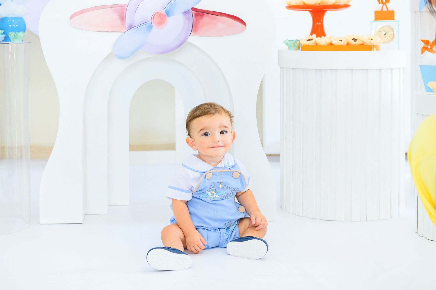 Small child in light blue outfit sits on white floor in front of decorative archway and playful decor.