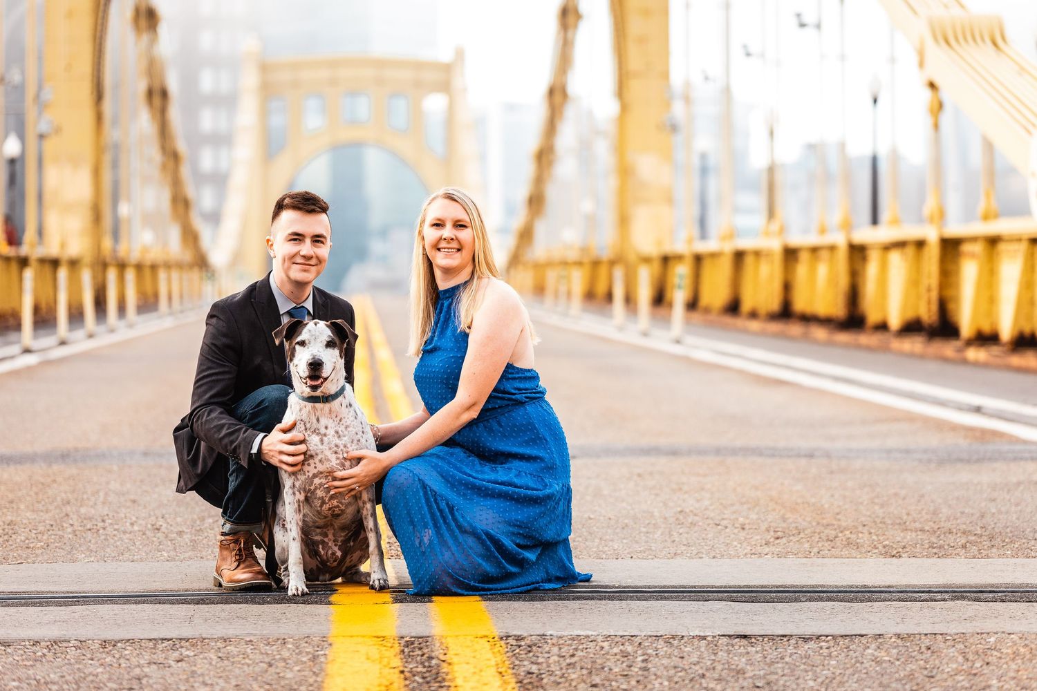 Couple poses with their Australian shepherd dog on yellow-lined bridge during golden hour photography session.