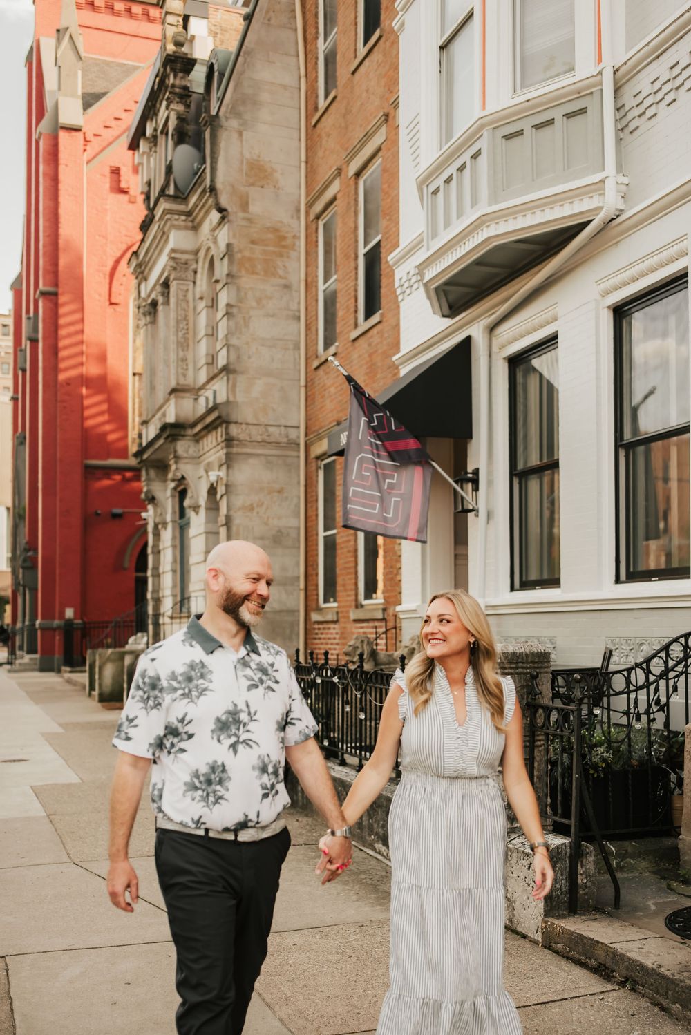 married couple holds hands and walks through over the rhine near Washington park in cincinnati