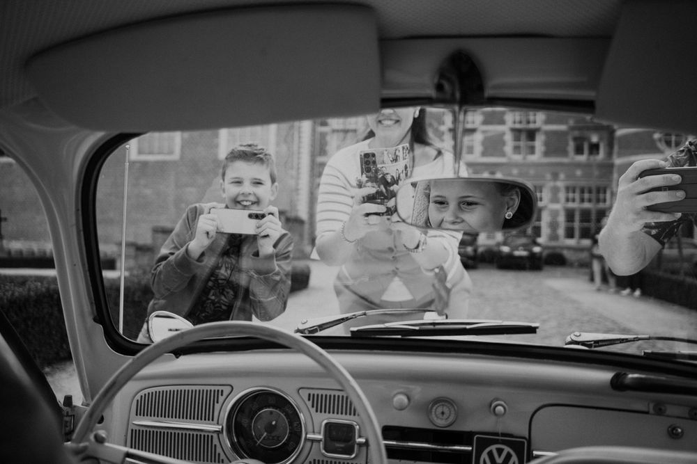 Een oude zwart-witfoto van een auto waarop drie mensen door de voorruit foto's nemen.