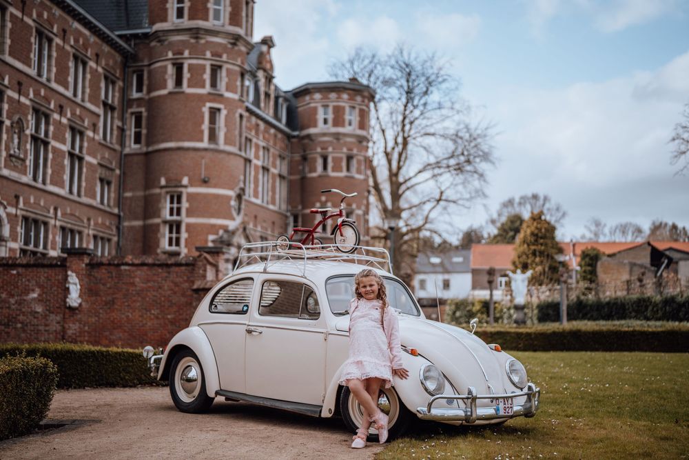 Klassieke witte Volkswagen Kever geparkeerd voor een groots bakstenen kasteel met torentjes op een zonnige herfstdag.