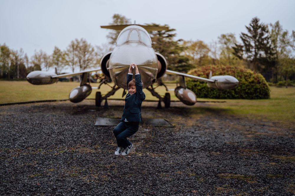 Militaire F-16 gevechtsvliegtuigen tentoongesteld in een park terwijl iemand vooraan een energieke springhouding aanneemt.