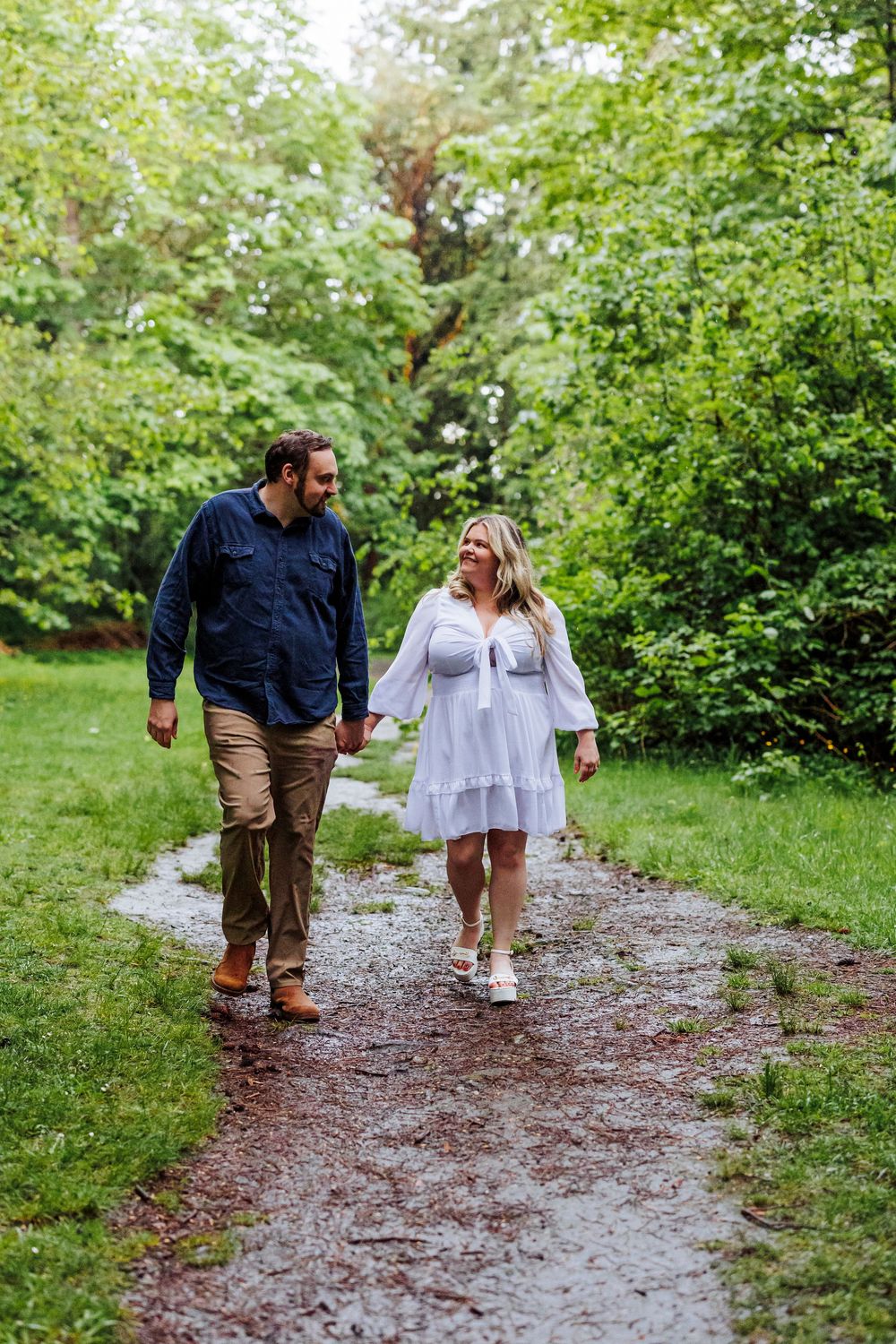 A couple walks together on a muddy trail through lush green foliage on a spring day.