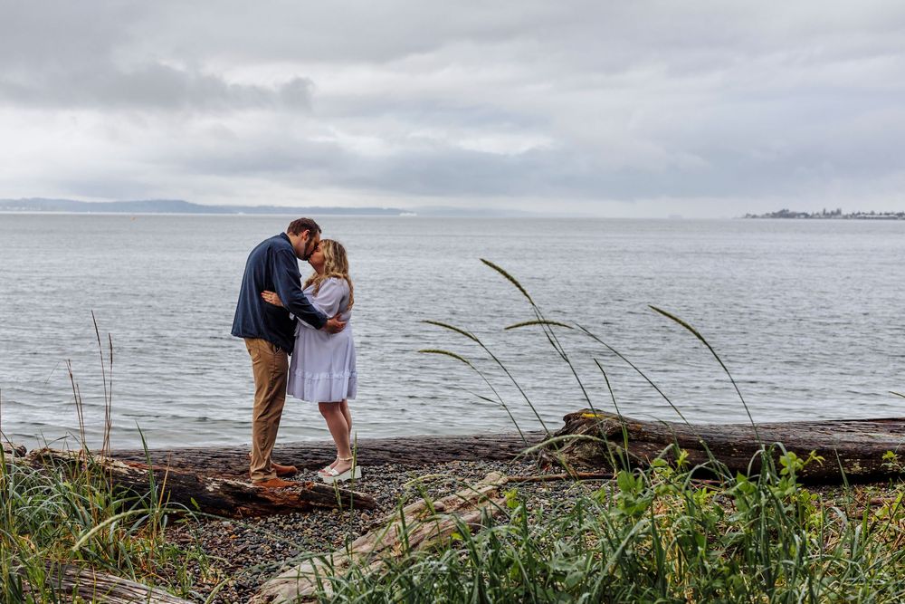 A romantic moment shared on a rocky coastal shoreline under moody cloudy skies.