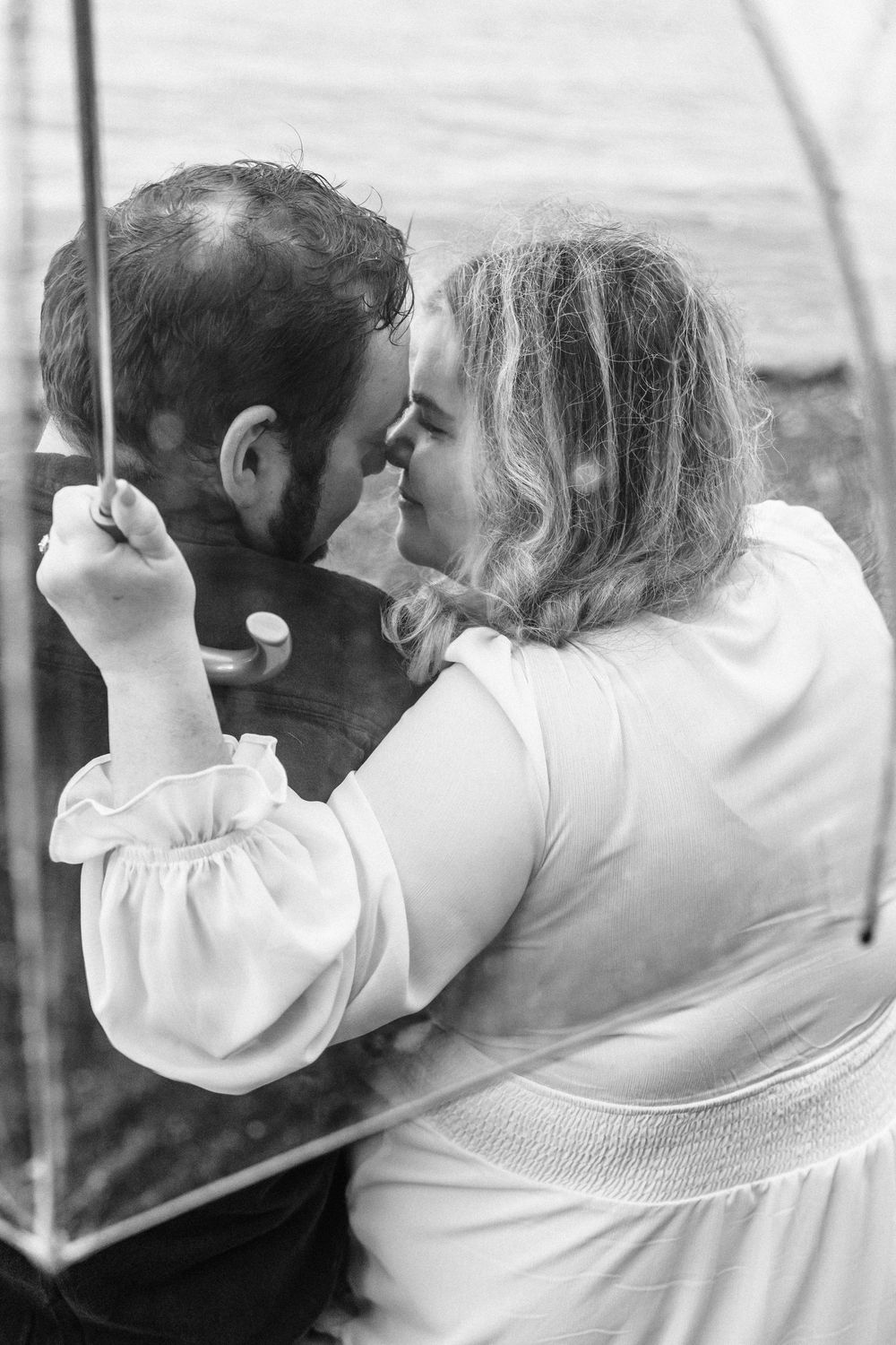 A romantic black and white photo of a couple sharing an intimate moment under an umbrella.