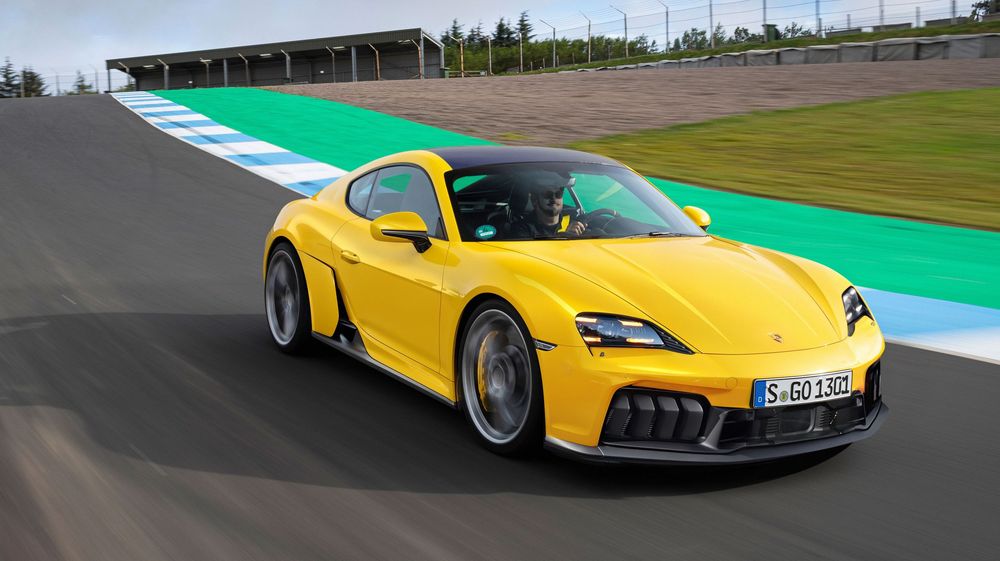 A bright yellow Porsche Cayman GT4 drives on a racetrack featuring green and blue curbing along the edge.