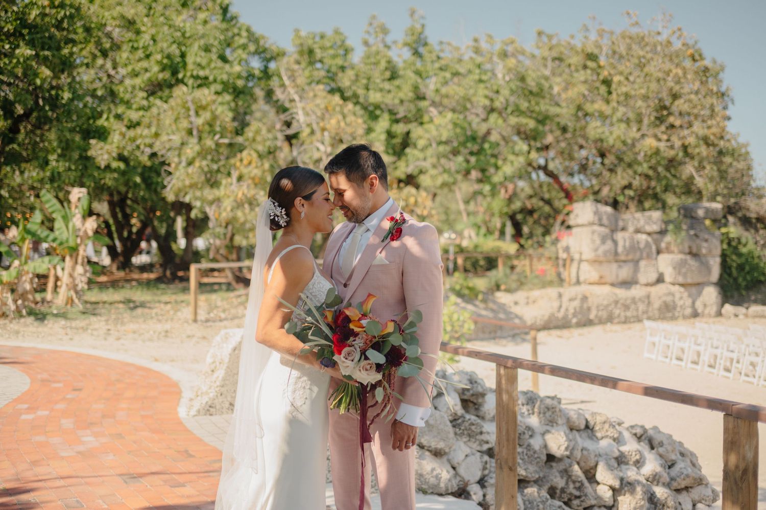 A couple shares an intimate moment at a rustic outdoor venue with stone walls and greenery in the background.