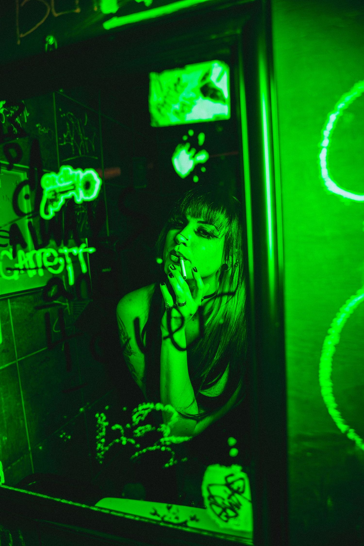 A dark moody scene with artistic green neon lighting illuminating someone through a mirror in a dive bar atmosphere.