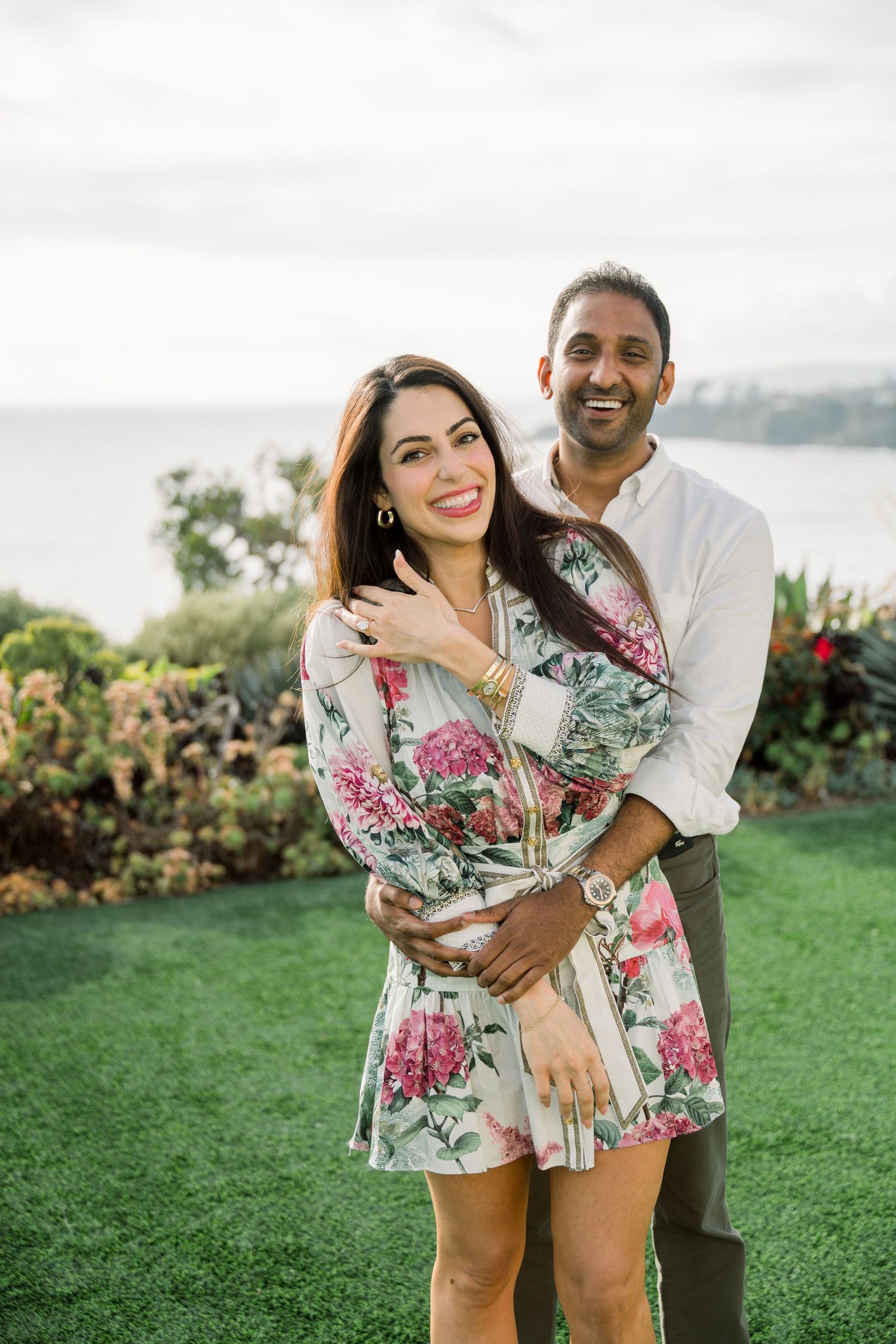 A romantic outdoor moment between two people embracing on grassy lawn, wearing a floral dress and white shirt.