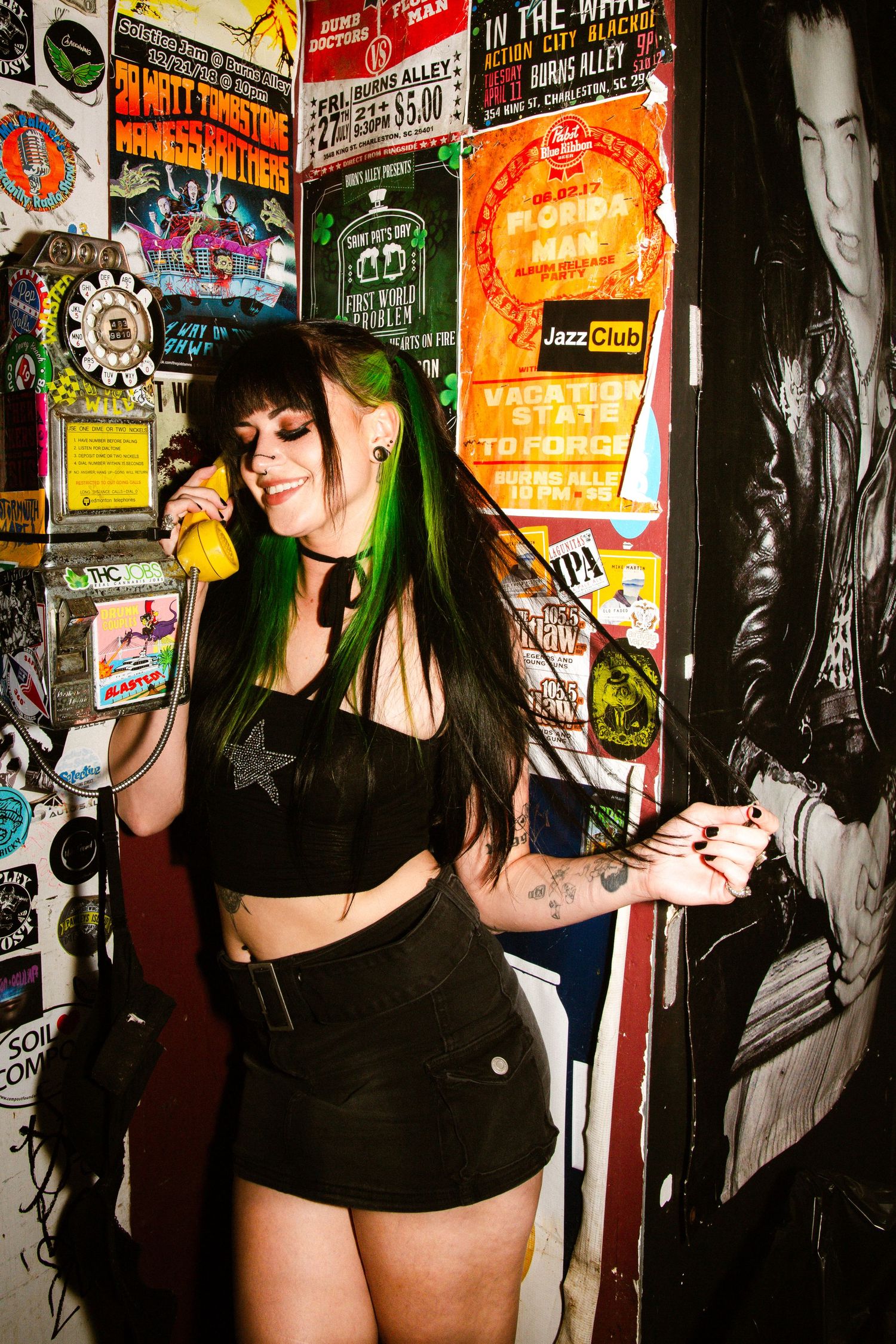 Alternative music scene captured at a venue with posters on wall, featuring dark clothing and concert promotional materials.