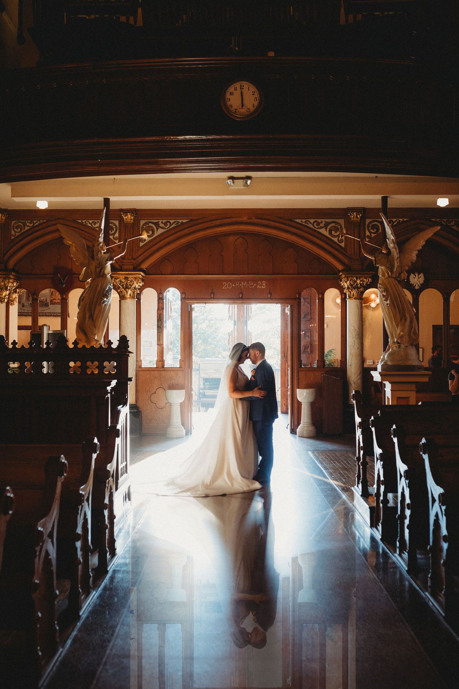 A romantic silhouette of a couple embracing in a historic church aisle with ornate wooden pews and streaming sunlight.