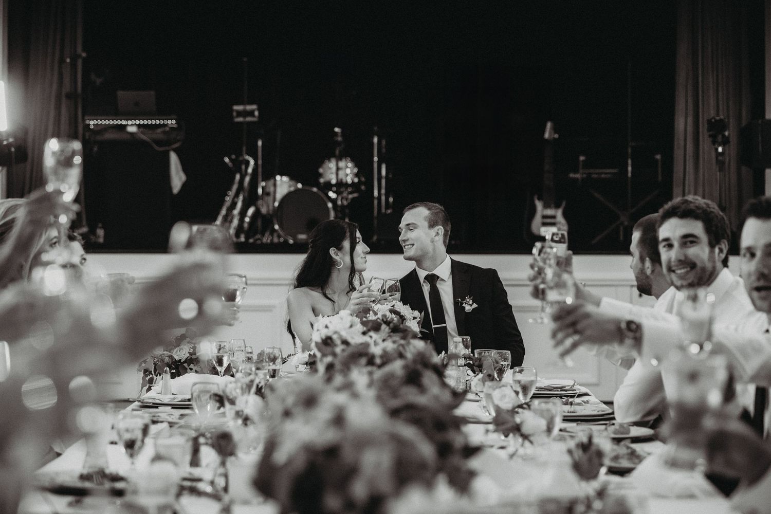 A candid black and white reception photo showing guests enjoying a formal dinner at an elegant table setting.