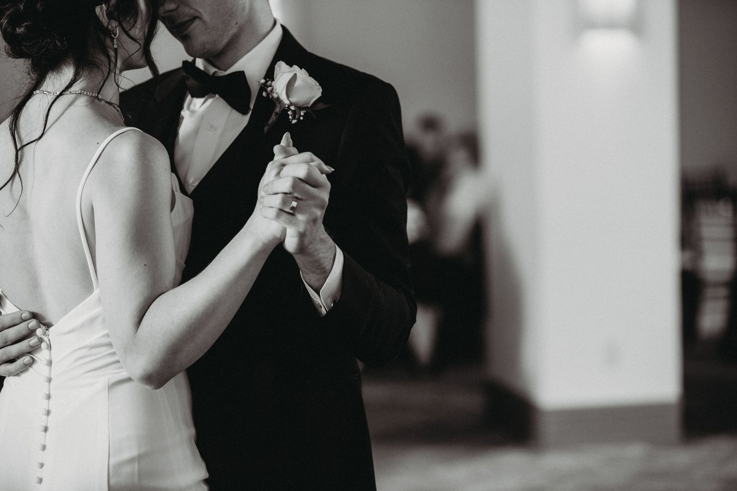 A black and white photo of a couple dancing together at their wedding reception in formal attire.