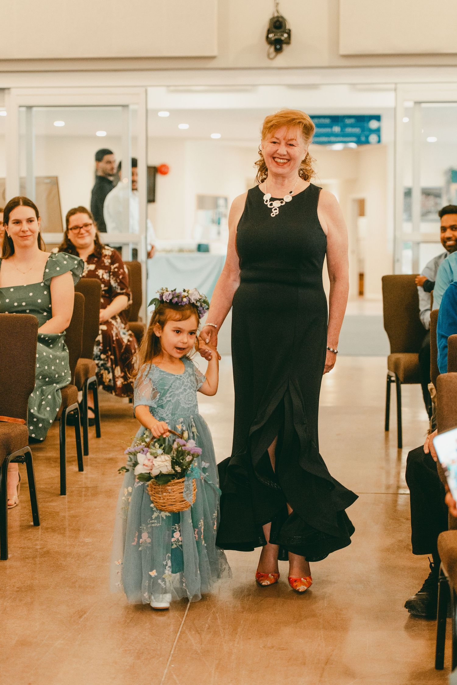 Happy mother of bride and cute flower girl walk down the aisle