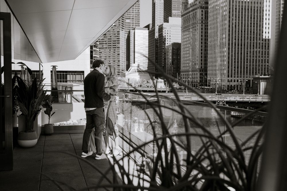 A silhouetted figure stands on a modern balcony overlooking city skyscrapers in black and white.