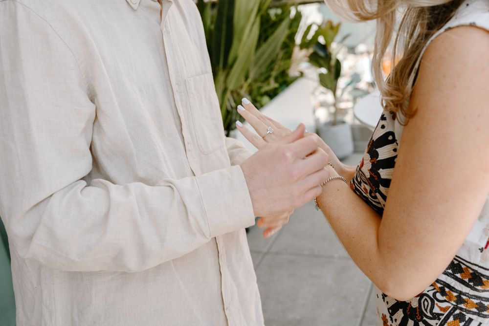 Two people hold hands during an intimate moment wearing light colored clothing against a blurred background.