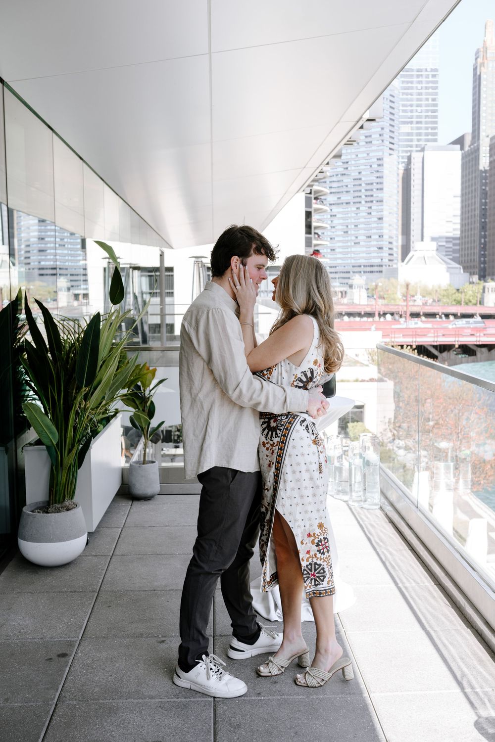 A romantic moment shared between a couple on a modern urban balcony with city views and potted plants.