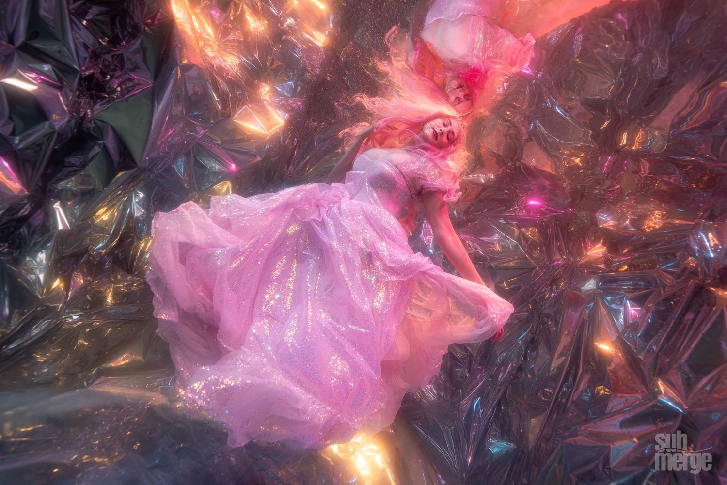 Underwater photography of a crumpled pink plastic bag illuminated with colorful reflections and lighting effects in a dark environment.