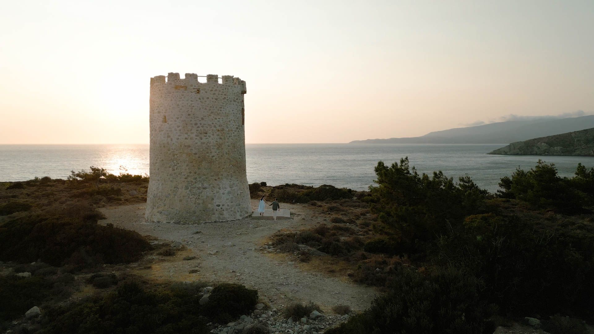 Ancient stone watchtower stands on a rocky coastal cliff at sunset overlooking a serene Mediterranean seascape.